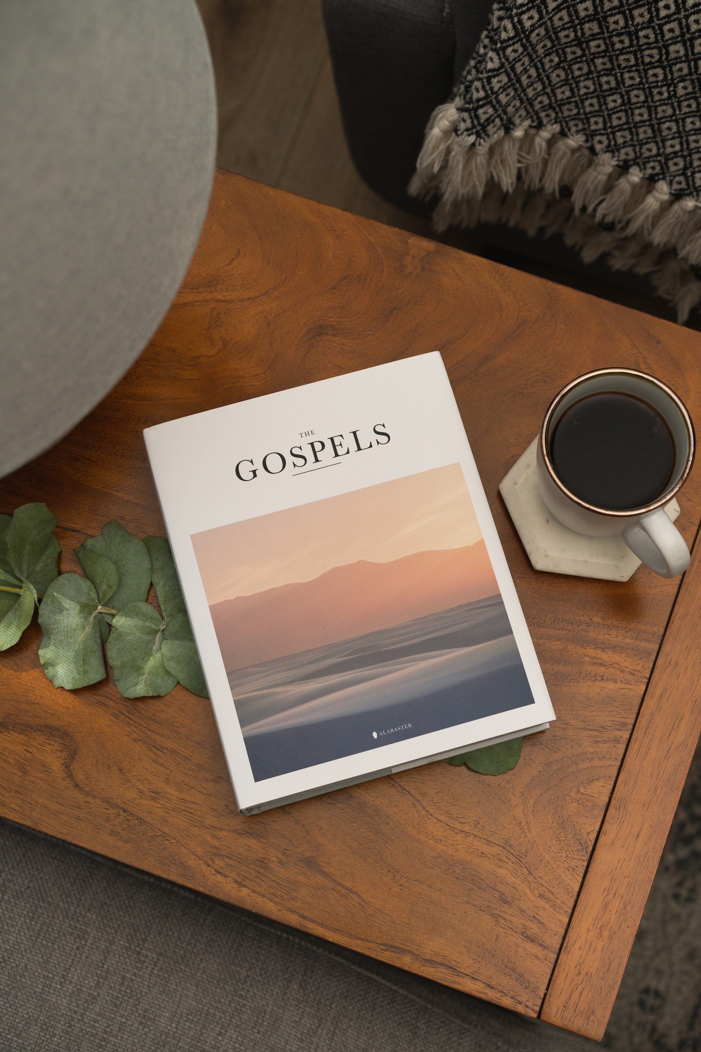 Alabaster's Gospels Hardcover on a coffee table by a cup of coffee