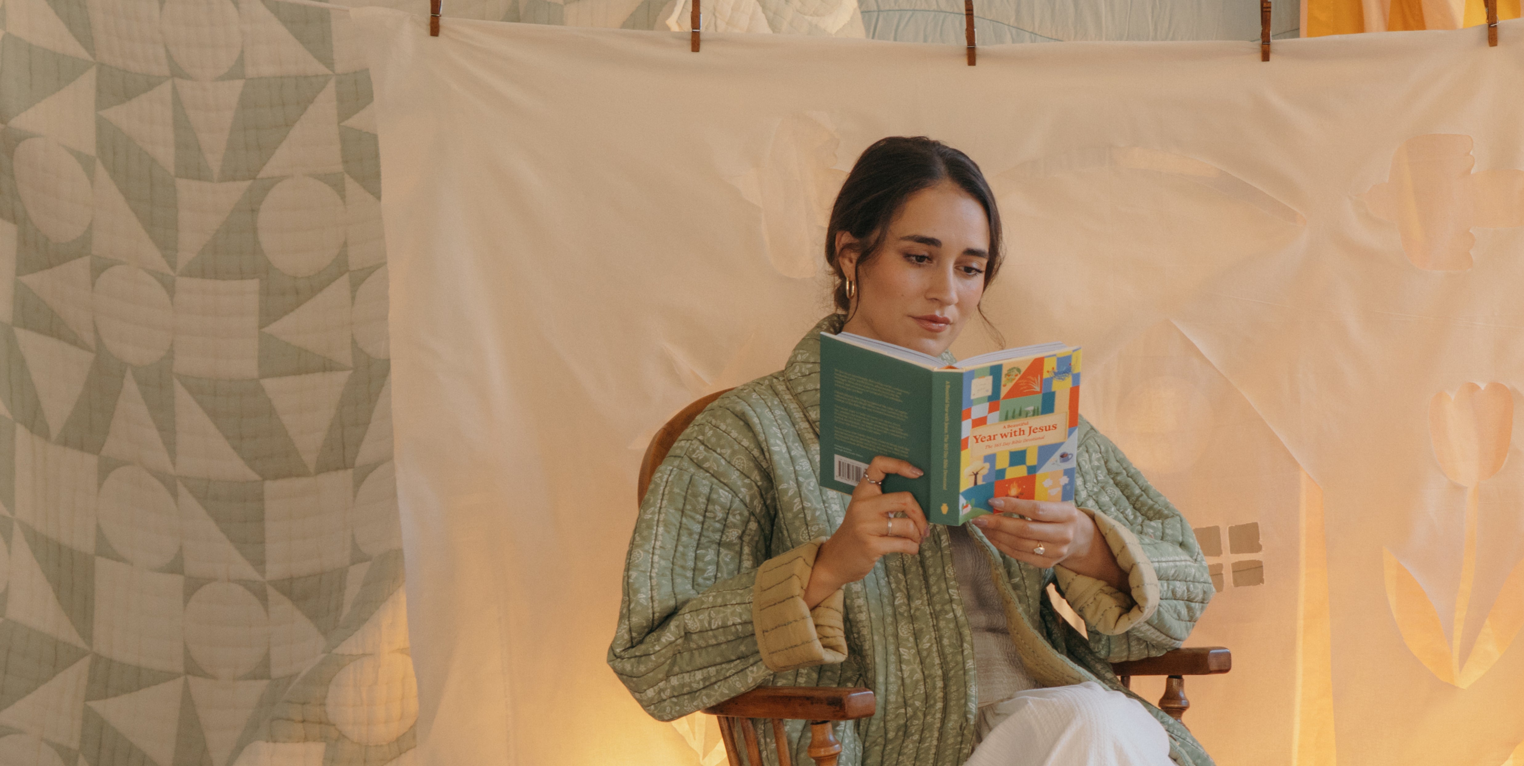 Woman reading a book in a cozy indoor setting with a patterned wall.